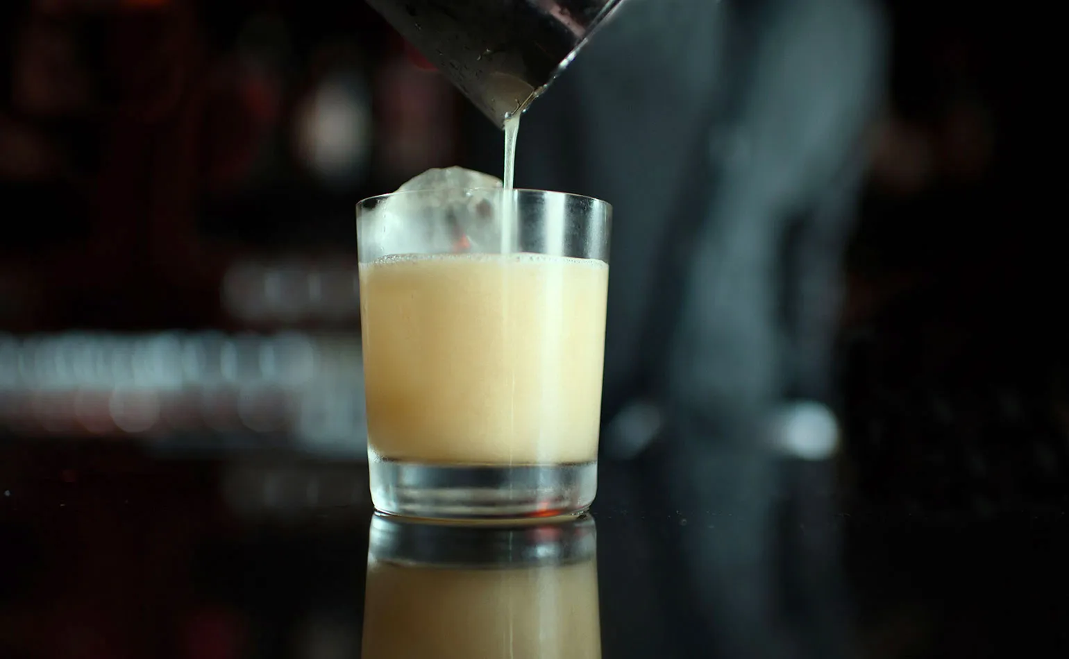 Hands holding a metal cocktail shaker mid-shake over a kitchen counter with lemons and a jigger nearby