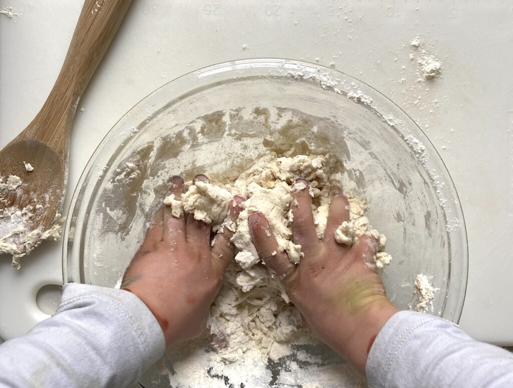 Hands kneading a smooth ball of salt dough on a lightly floured kitchen counter under warm lighting
