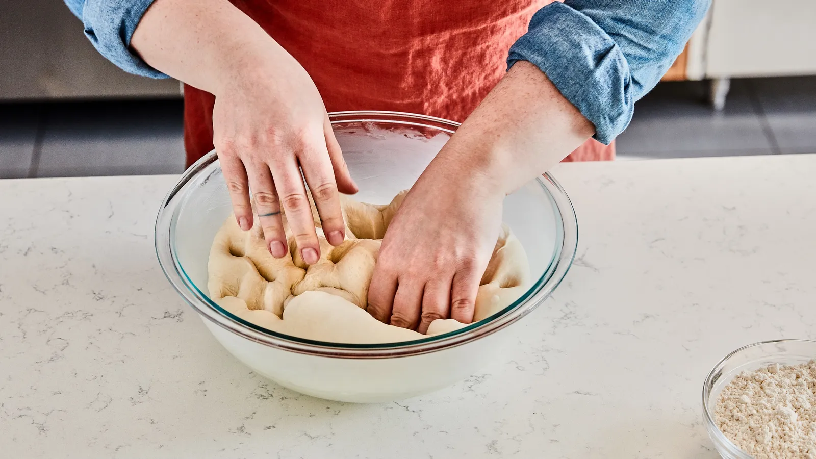 Hands kneading a smooth, slightly tacky milk bread dough on a lightly floured wooden countertop