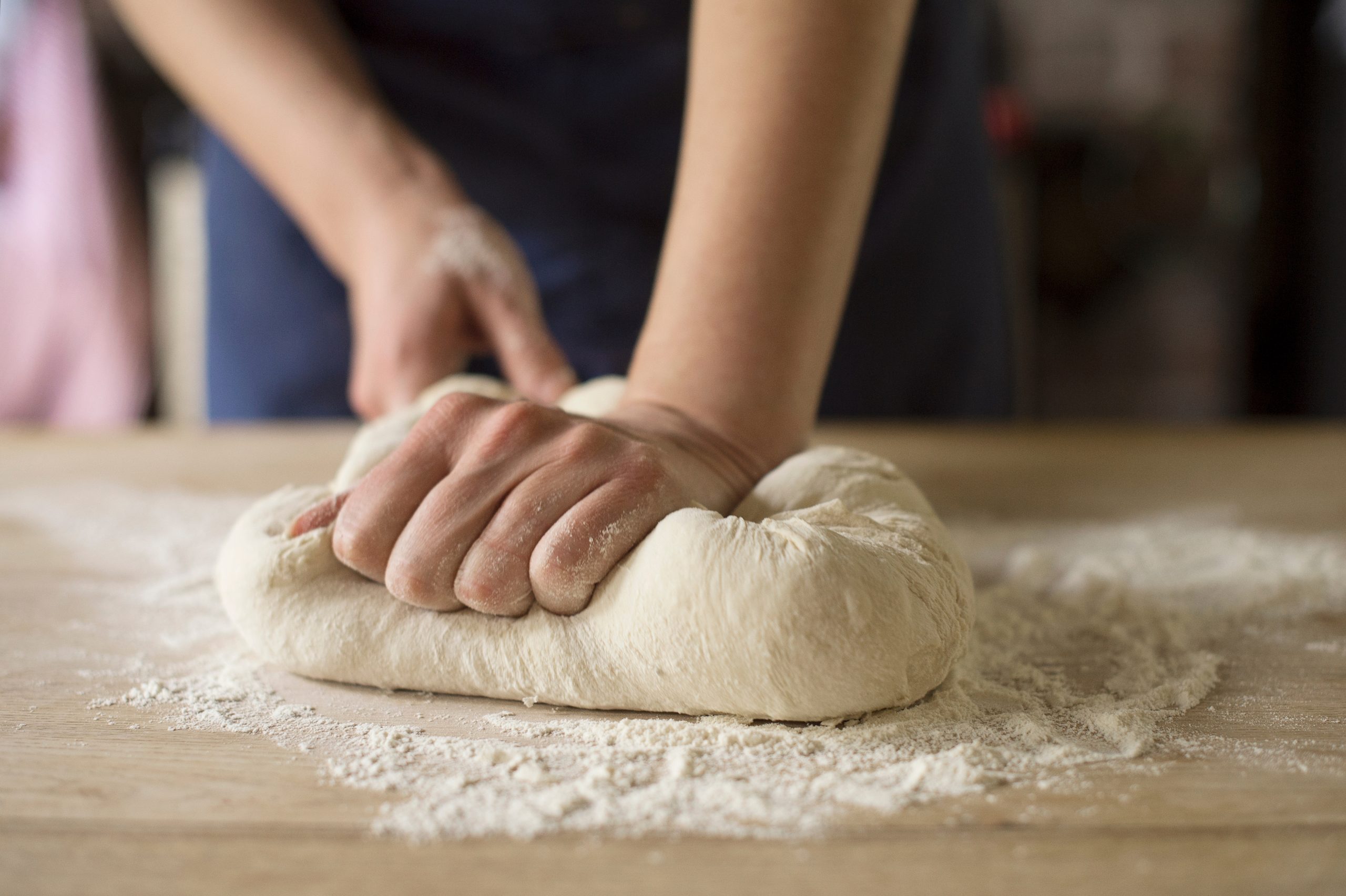 Hands kneading a soft bread dough on a lightly floured countertop in a home kitchen