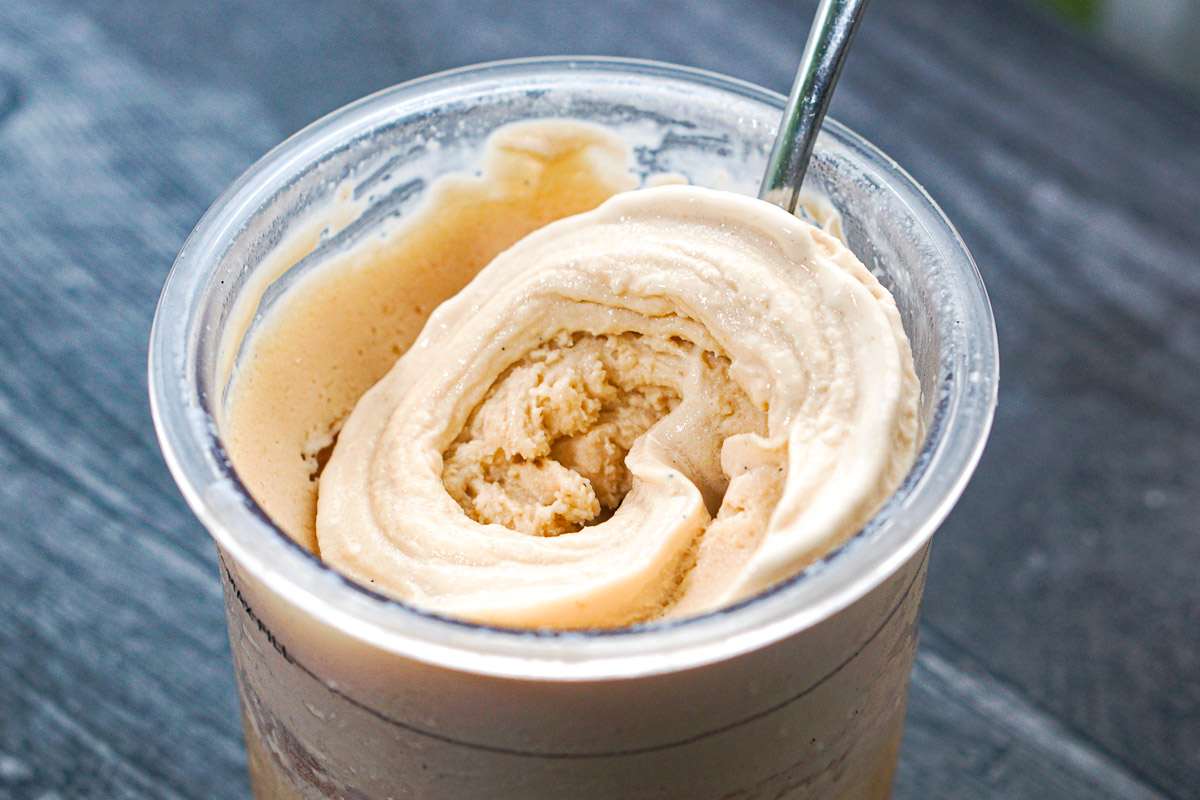 Hands measuring milk, cream, sugar, and vanilla into a Ninja Creami pint on a clean kitchen counter