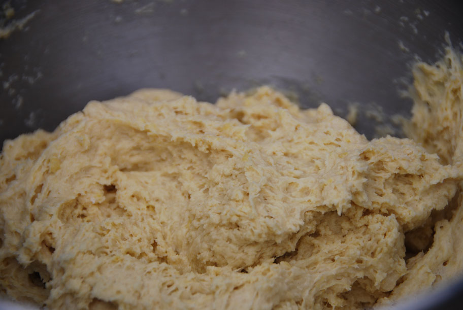 Hands mixing buñuelos dough in a large bowl on a home kitchen counter with flour and eggs visible, warm natural light