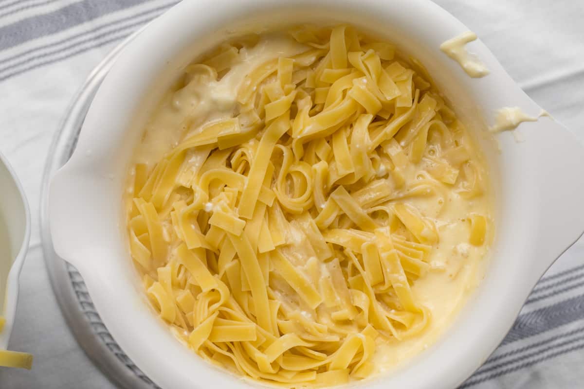 Hands mixing eggs, sour cream, and cottage cheese in a large mixing bowl on a home kitchen counter