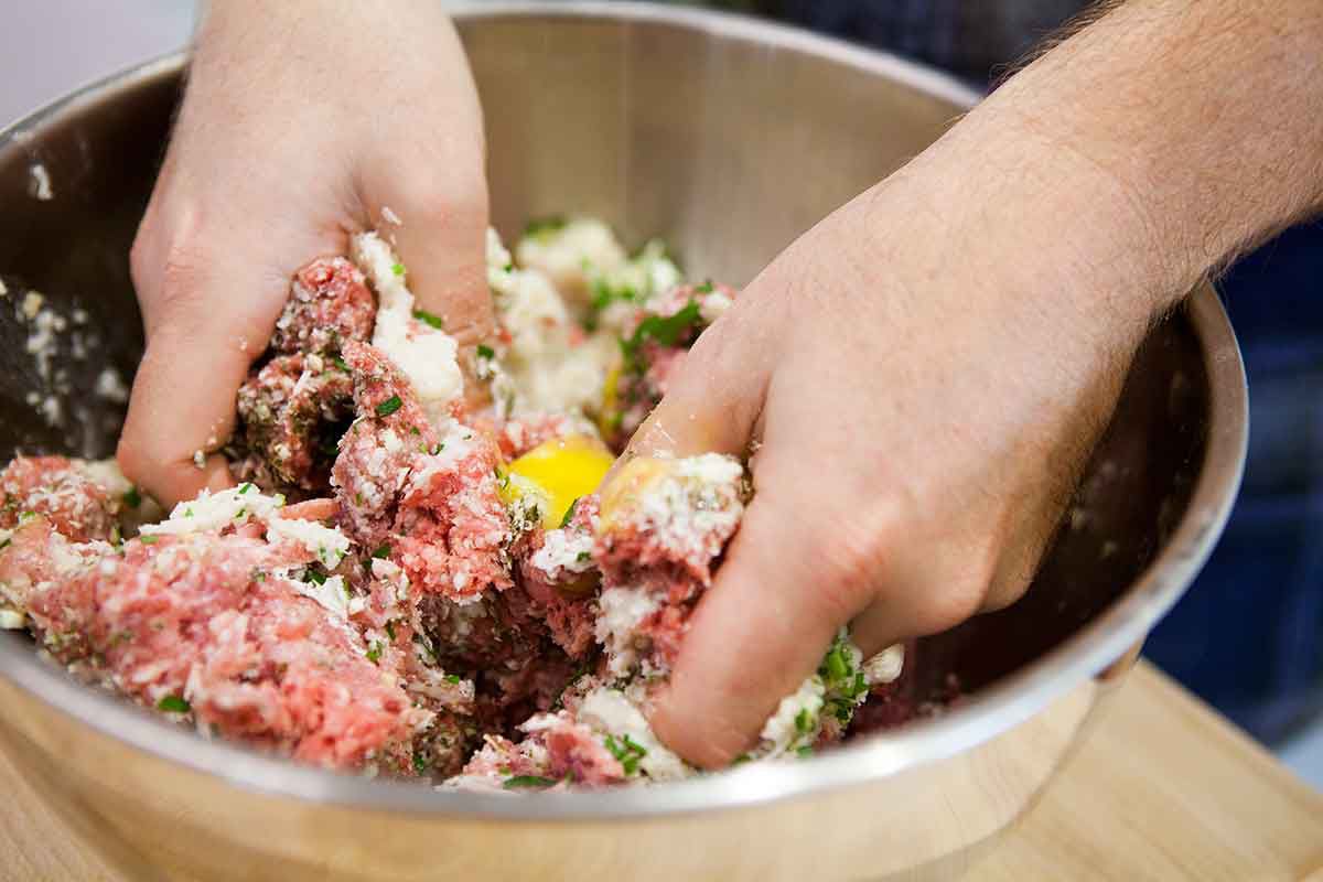Hands mixing ground beef meatball mixture in a large bowl on a kitchen counter