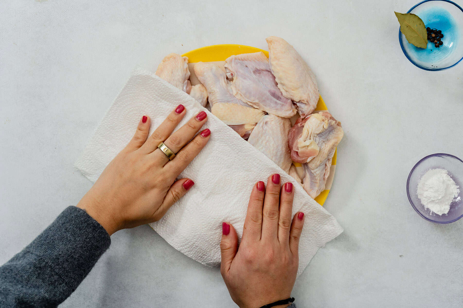 Hands patting chicken wings dry with paper towels on a baking sheet in a bright home kitchen