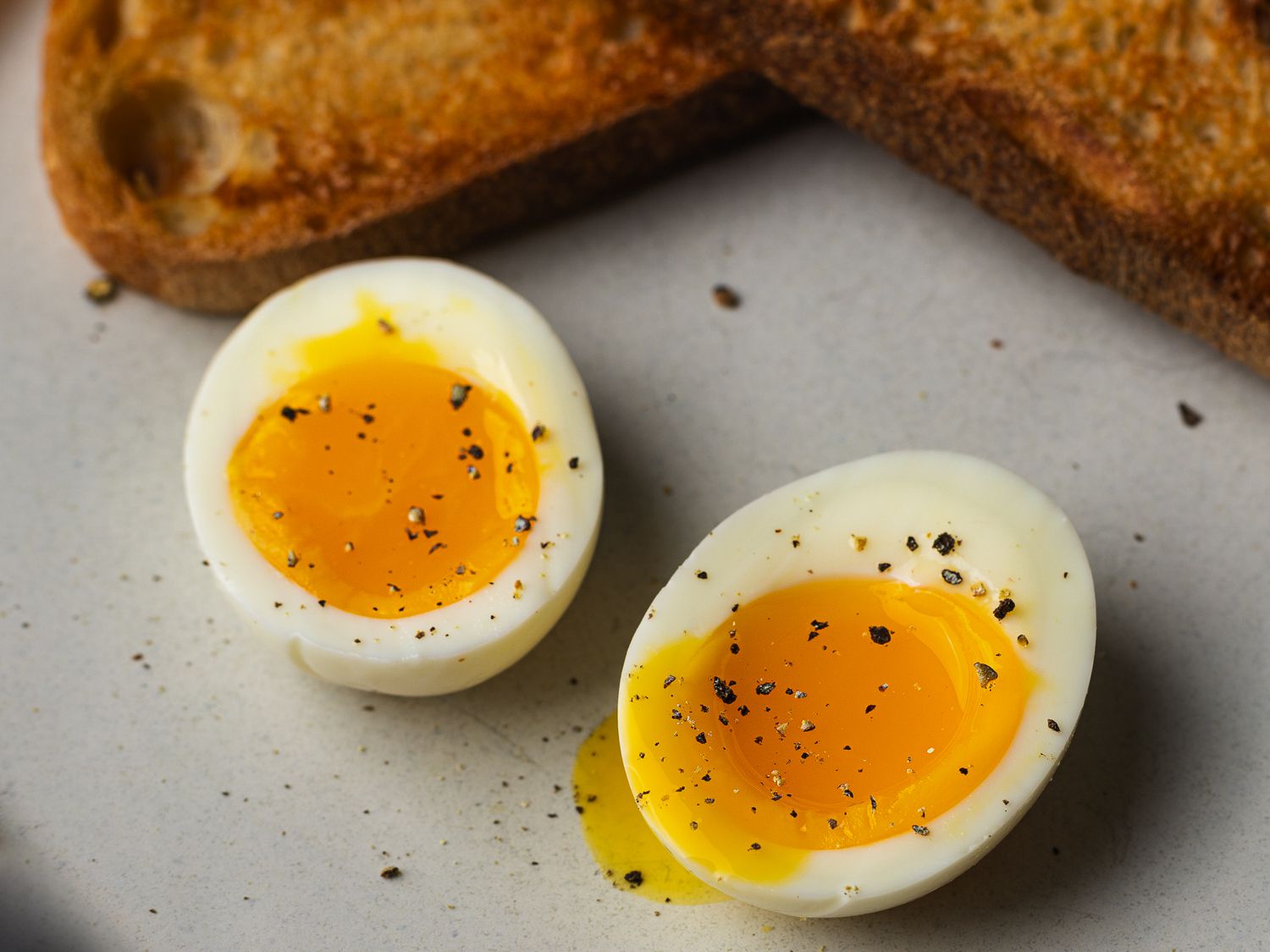 Hands peeling a soft-boiled egg under running water at a kitchen sink, with shell fragments falling away cleanly
