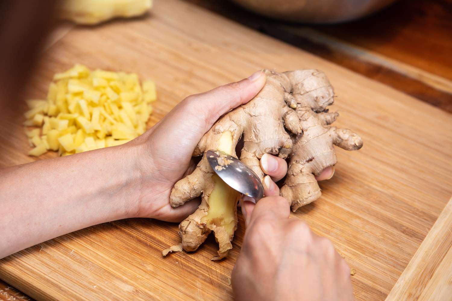 Hands peeling fresh ginger with a spoon over a cutting board on a kitchen counter in natural light