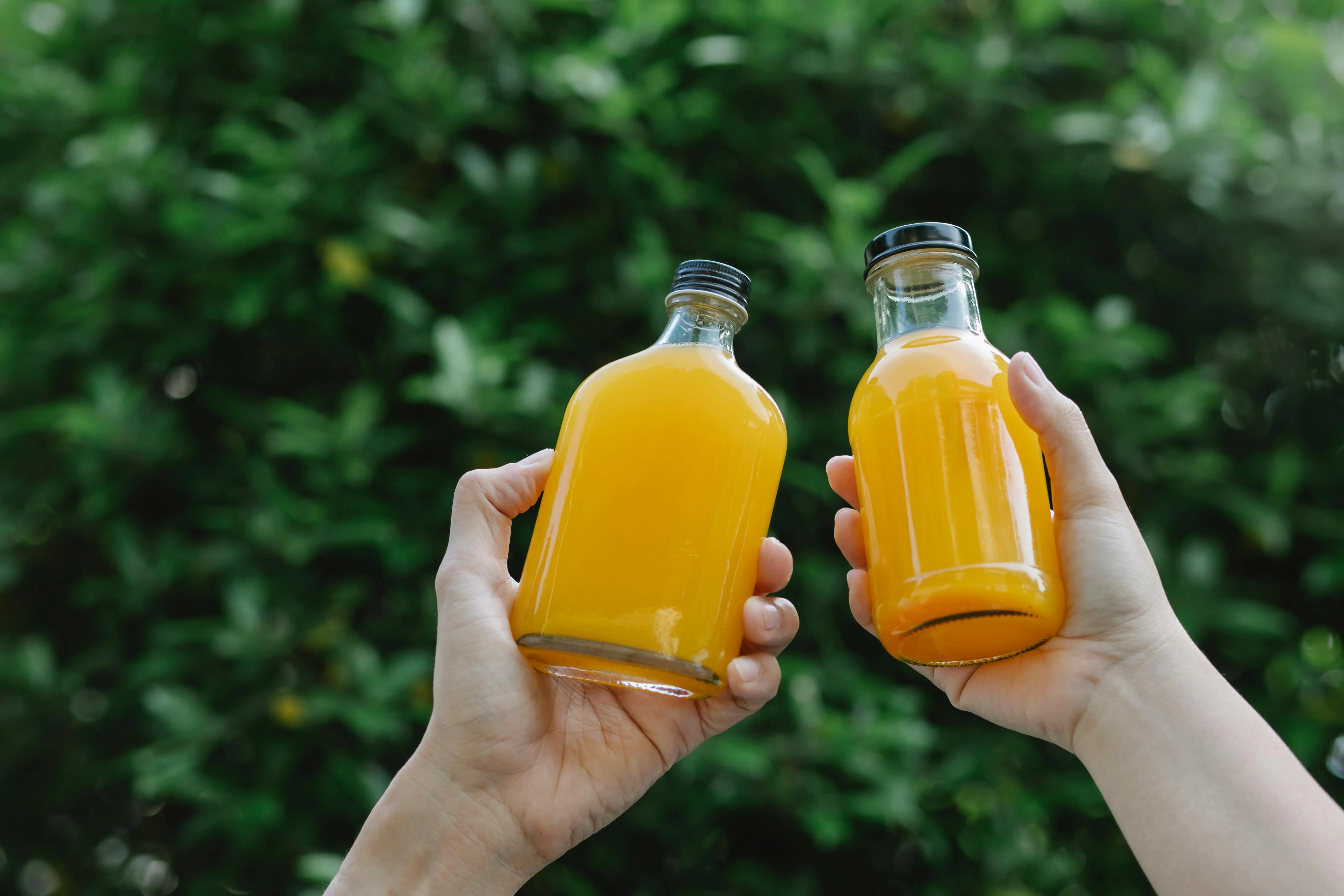 Hands pouring freshly blended juice through a fine mesh strainer into small glass bottles on a kitchen counter