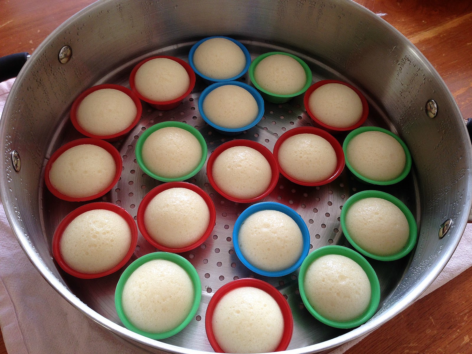 Hands pouring puto batter into small greased puto molds arranged on a steamer rack