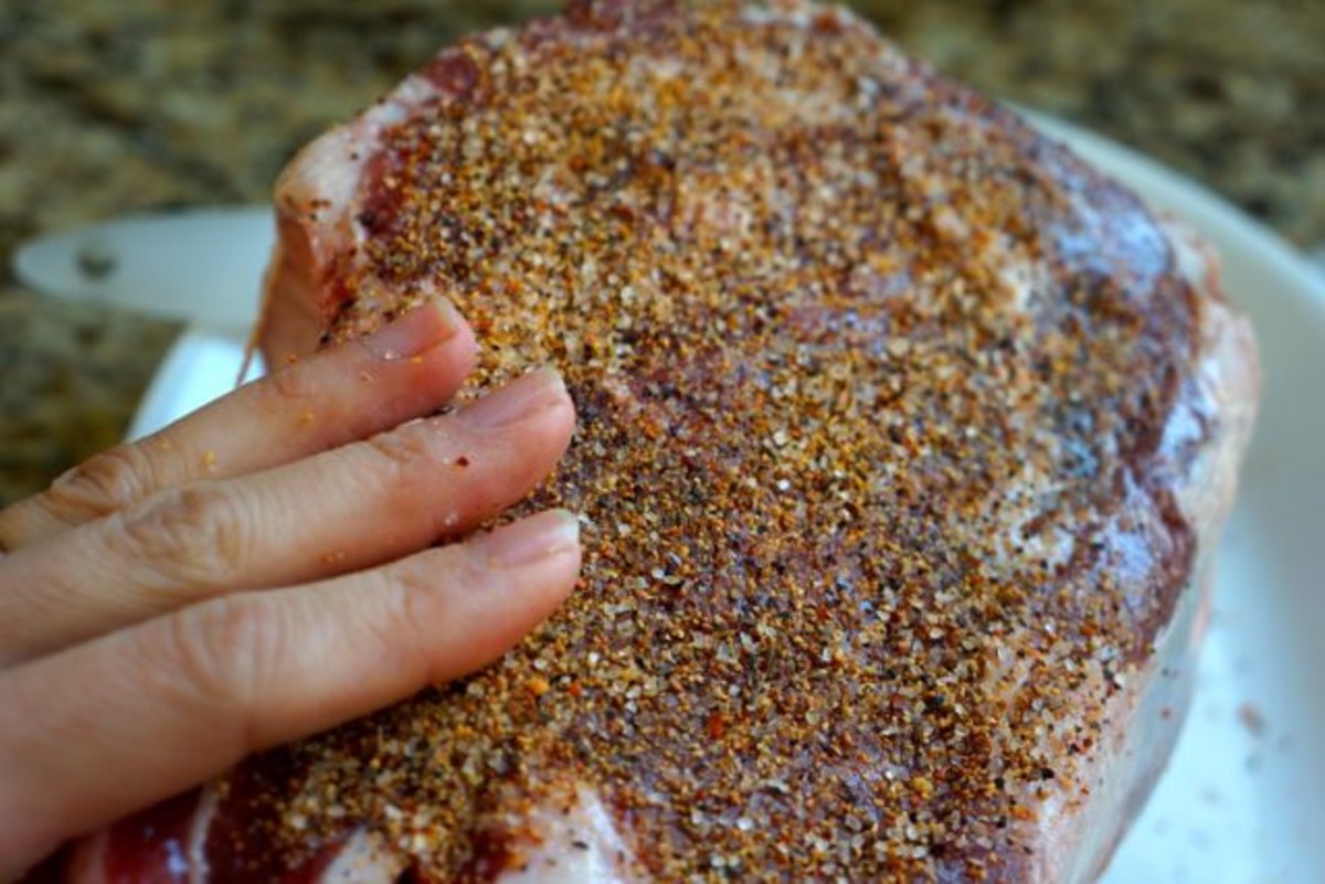 Hands pressing a peppery herb seasoning blend onto a prime rib roast on a cutting board