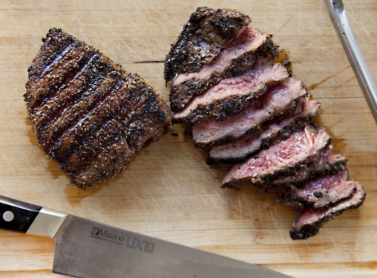 Hands pressing coarsely cracked black pepper onto the surface of a raw steak on a wooden cutting board