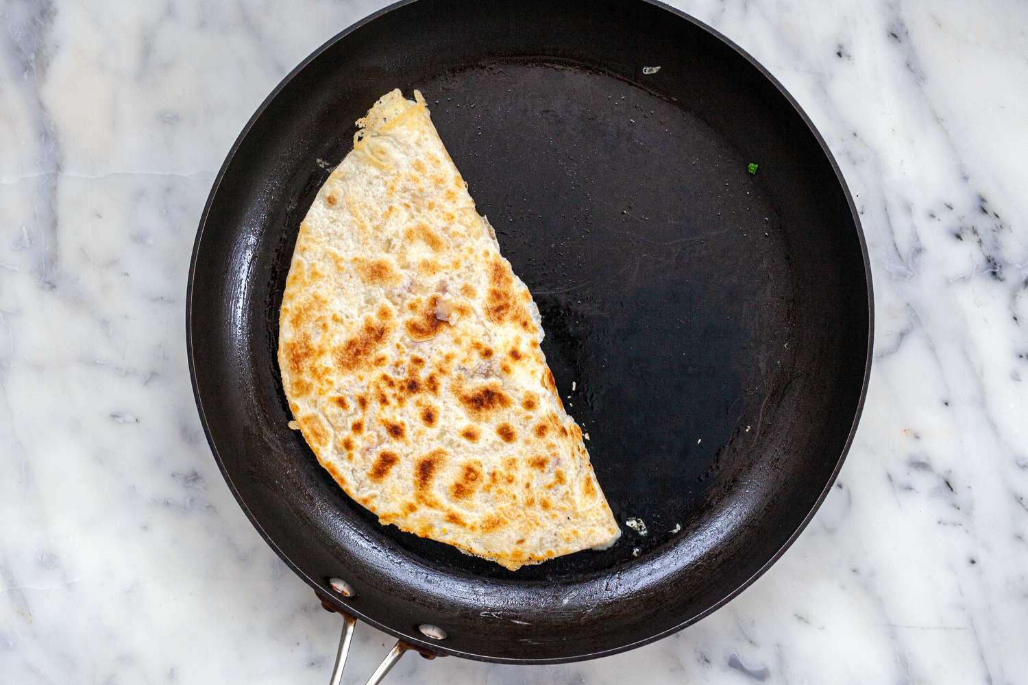Hands pressing down on a quesadilla with a spatula in a skillet as the tortilla browns