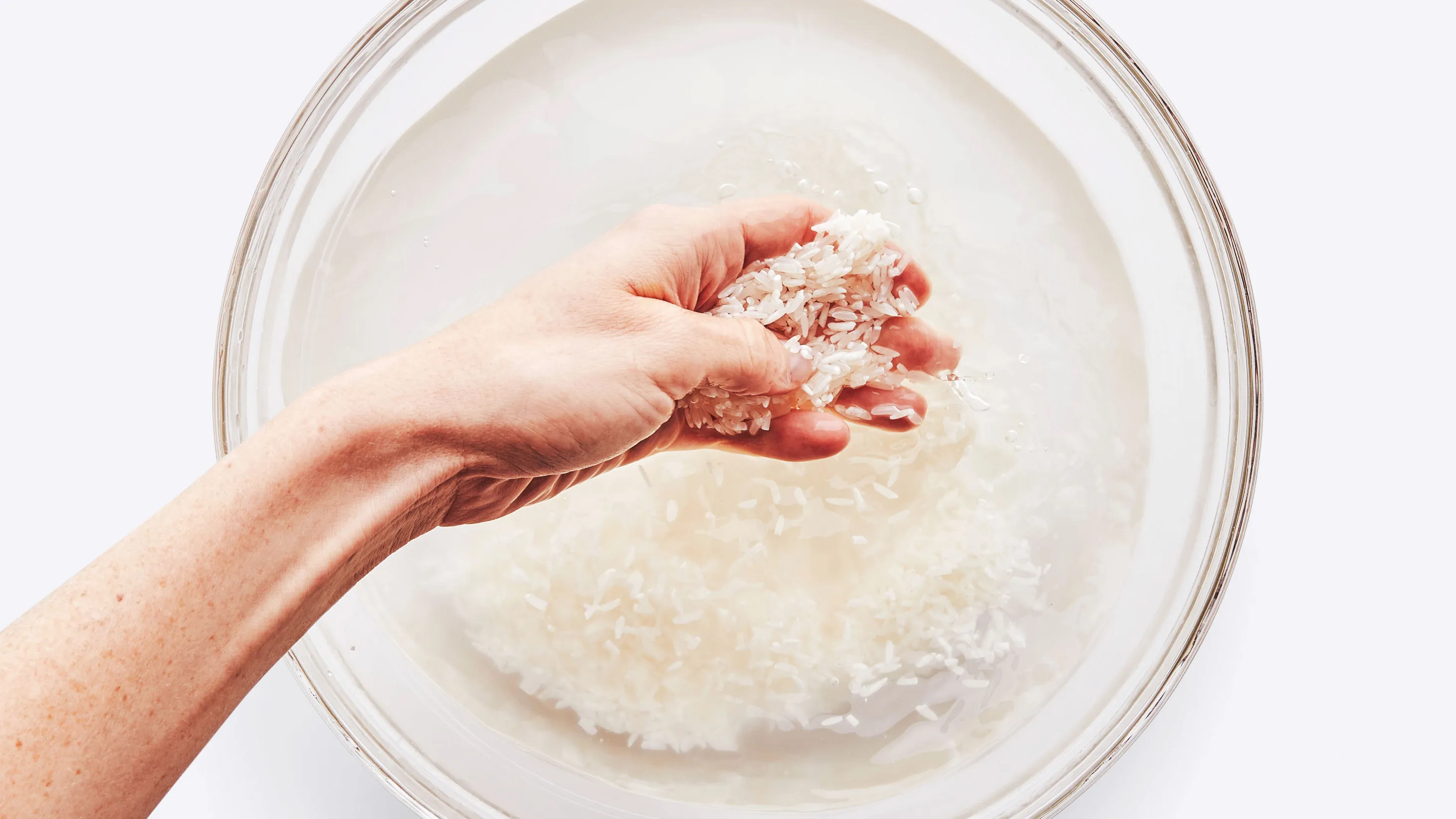 Hands rinsing basmati rice in a fine mesh strainer under a kitchen faucet, water running clear into a sink