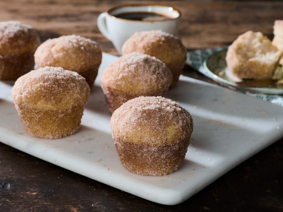 Hands rolling a warm muffin in a bowl of cinnamon sugar on a kitchen counter
