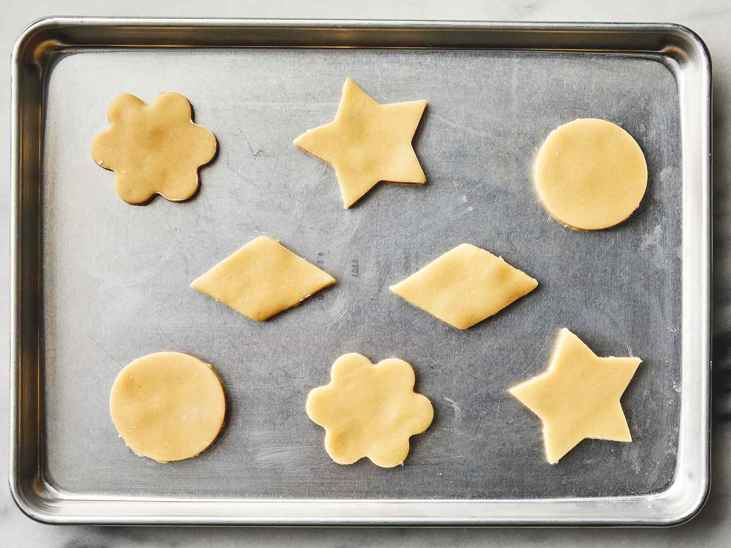 Hands rolling chilled sugar cookie dough on a lightly floured countertop with a wooden rolling pin