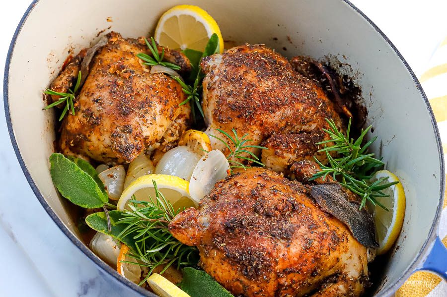 Hands rubbing softened herb butter and seasoning over a raw Cornish game hen on a sheet pan in a home kitchen
