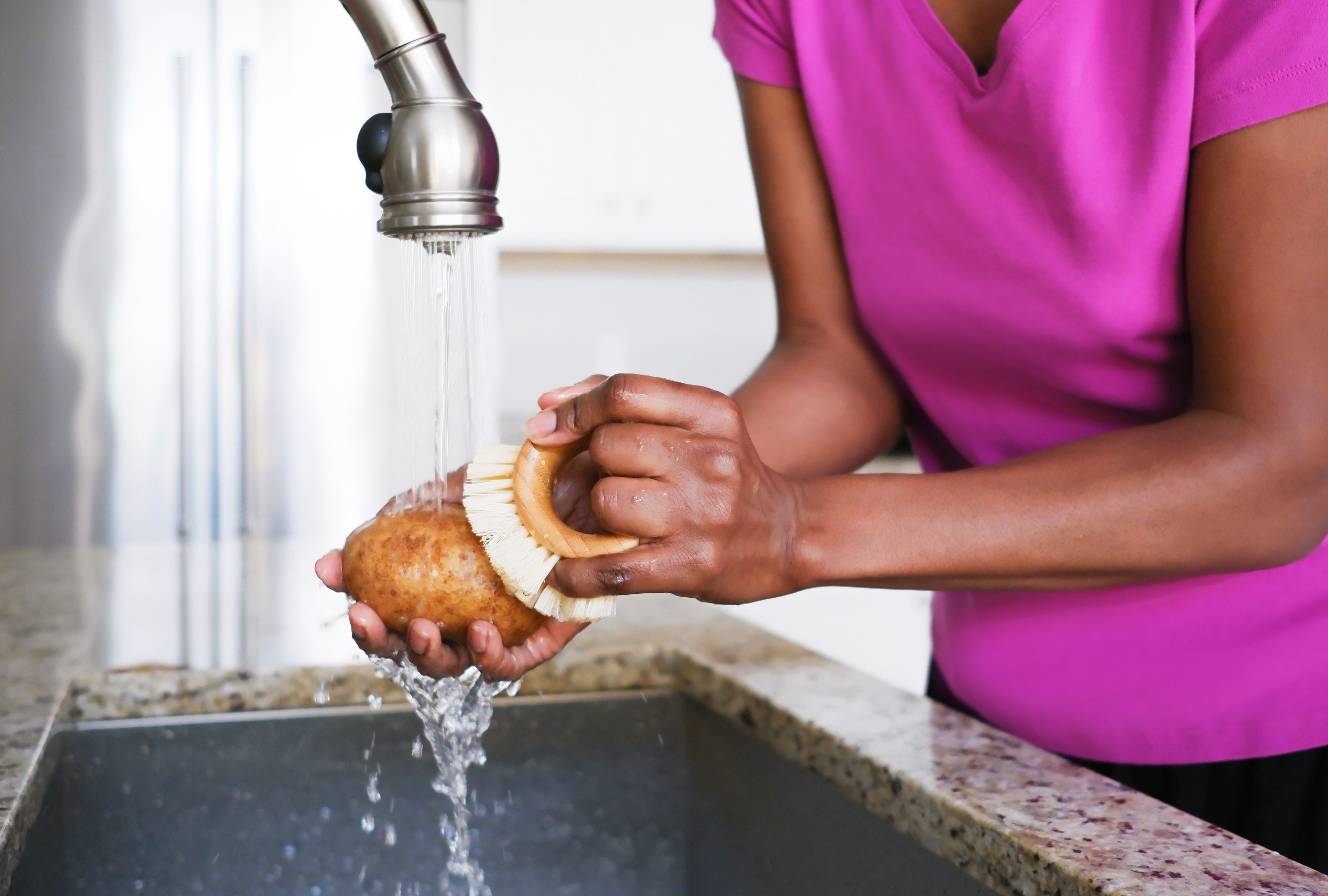 Hands scrubbing sweet potatoes under running water at a kitchen sink