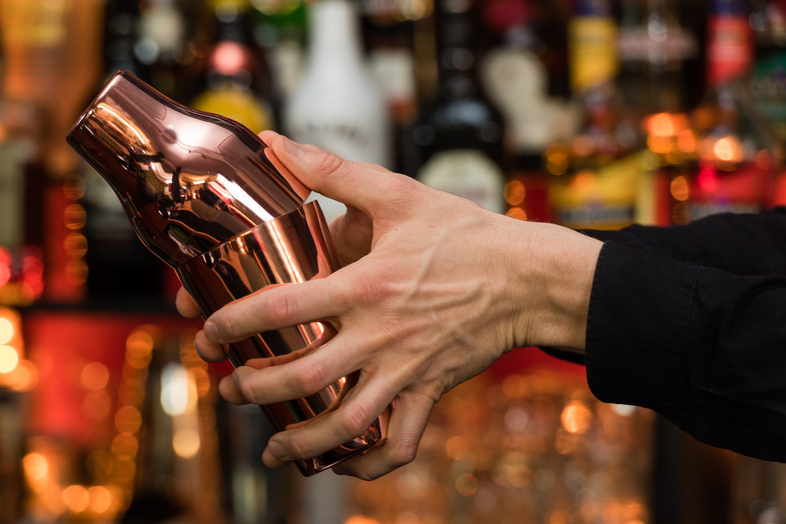 Hands shaking a stainless steel cocktail shaker over a kitchen counter with a prepared salt-rimmed glass nearby
