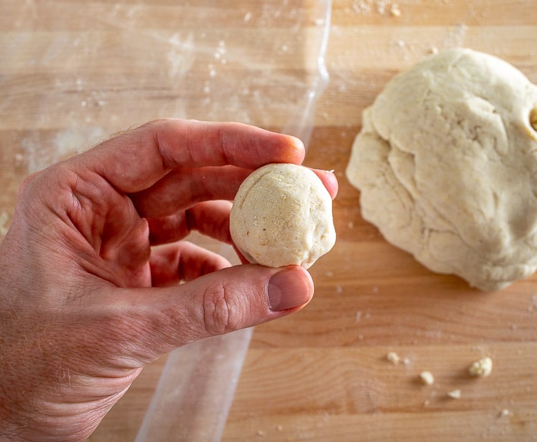 Hands shaping a smooth ball of masa dough in a mixing bowl on a kitchen counter