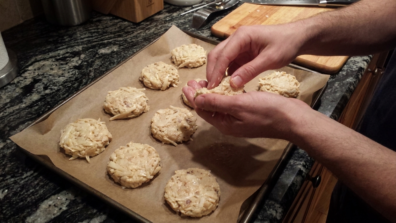 Hands shaping hearts of palm mixture into small patties on a parchment-lined baking sheet on a home kitchen counter