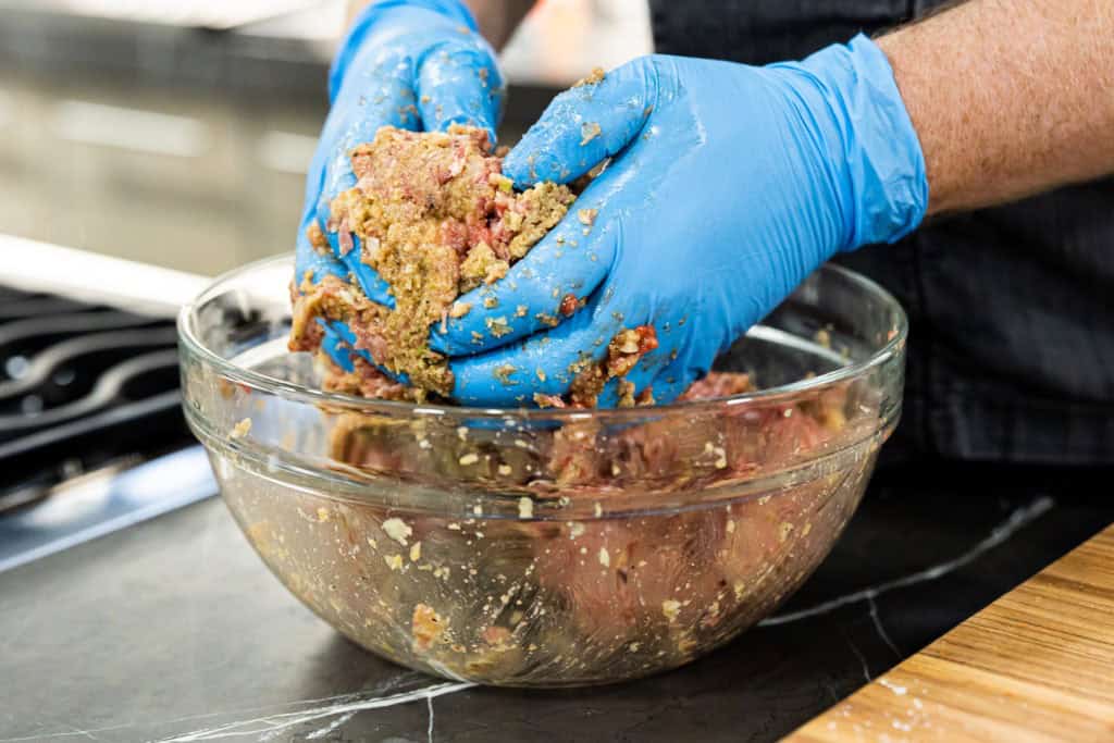 Hands shaping seasoned meatloaf mixture into a loaf on foil