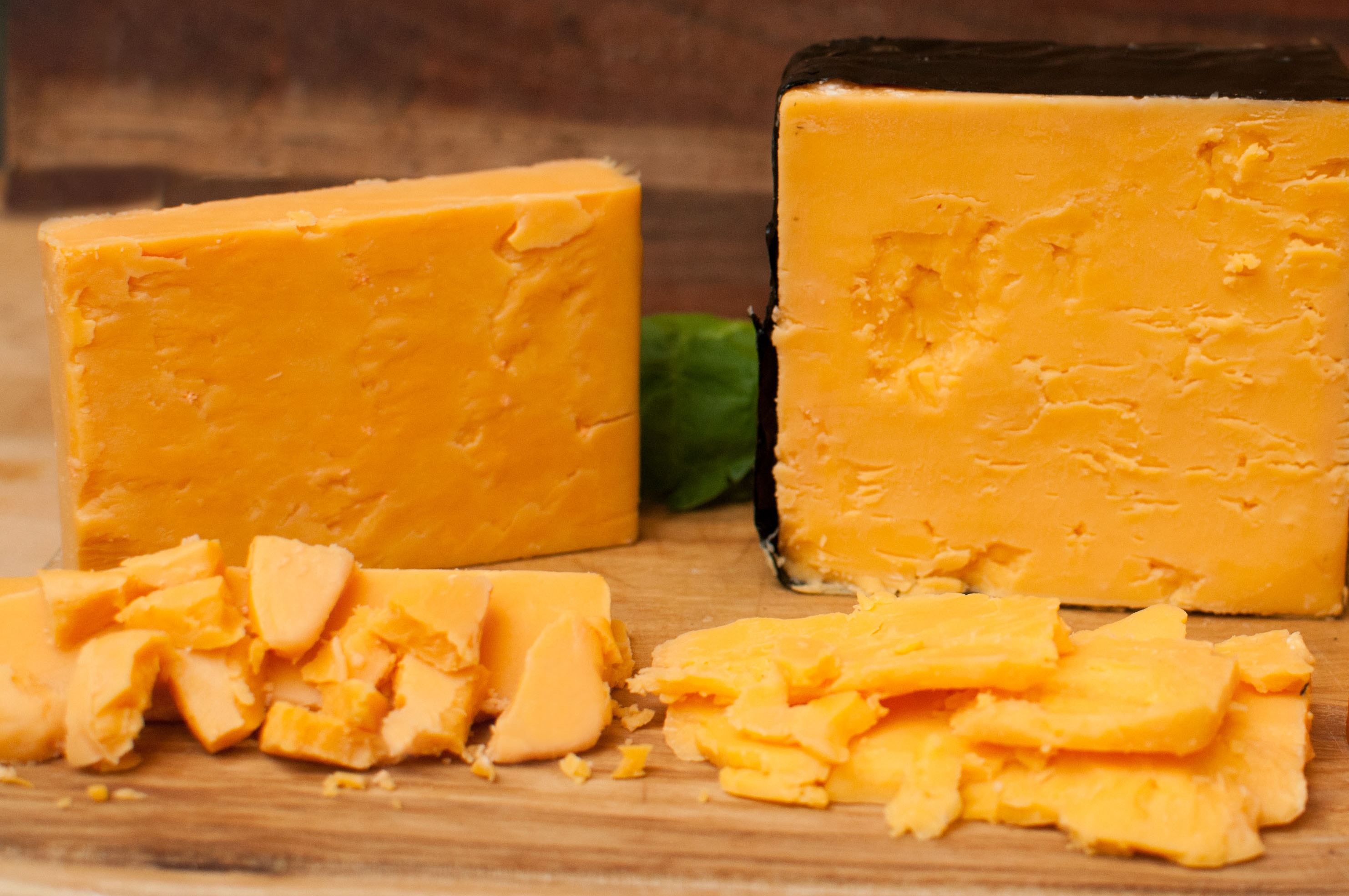 Hands shredding a block of sharp cheddar on a box grater over a mixing bowl on a bright kitchen counter