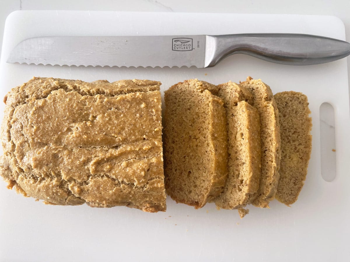 Hands slicing a cooled almond flour bread loaf with a serrated knife on a cutting board, showing a tender crumb