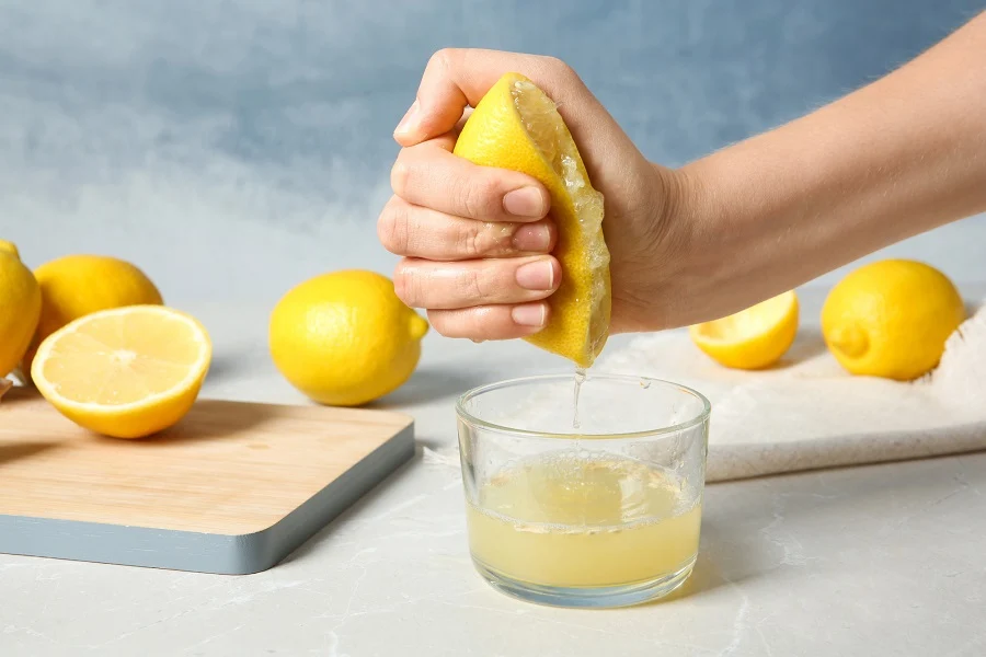 Hands squeezing a fresh lemon over a small bowl on a kitchen counter, with a simple citrus juicer nearby