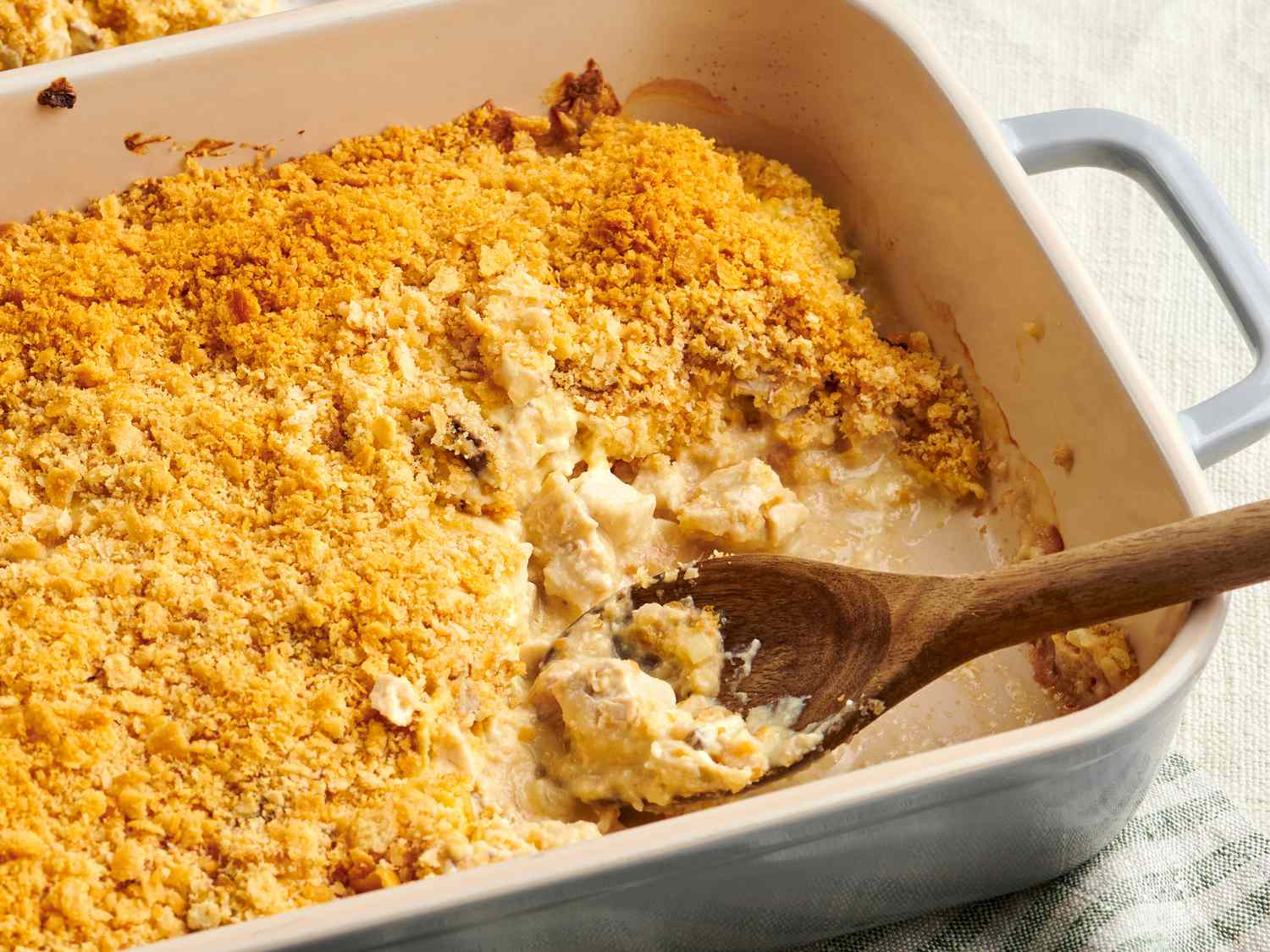 Hands stirring a creamy chicken and cheese mixture in a large bowl with a rubber spatula on a kitchen counter