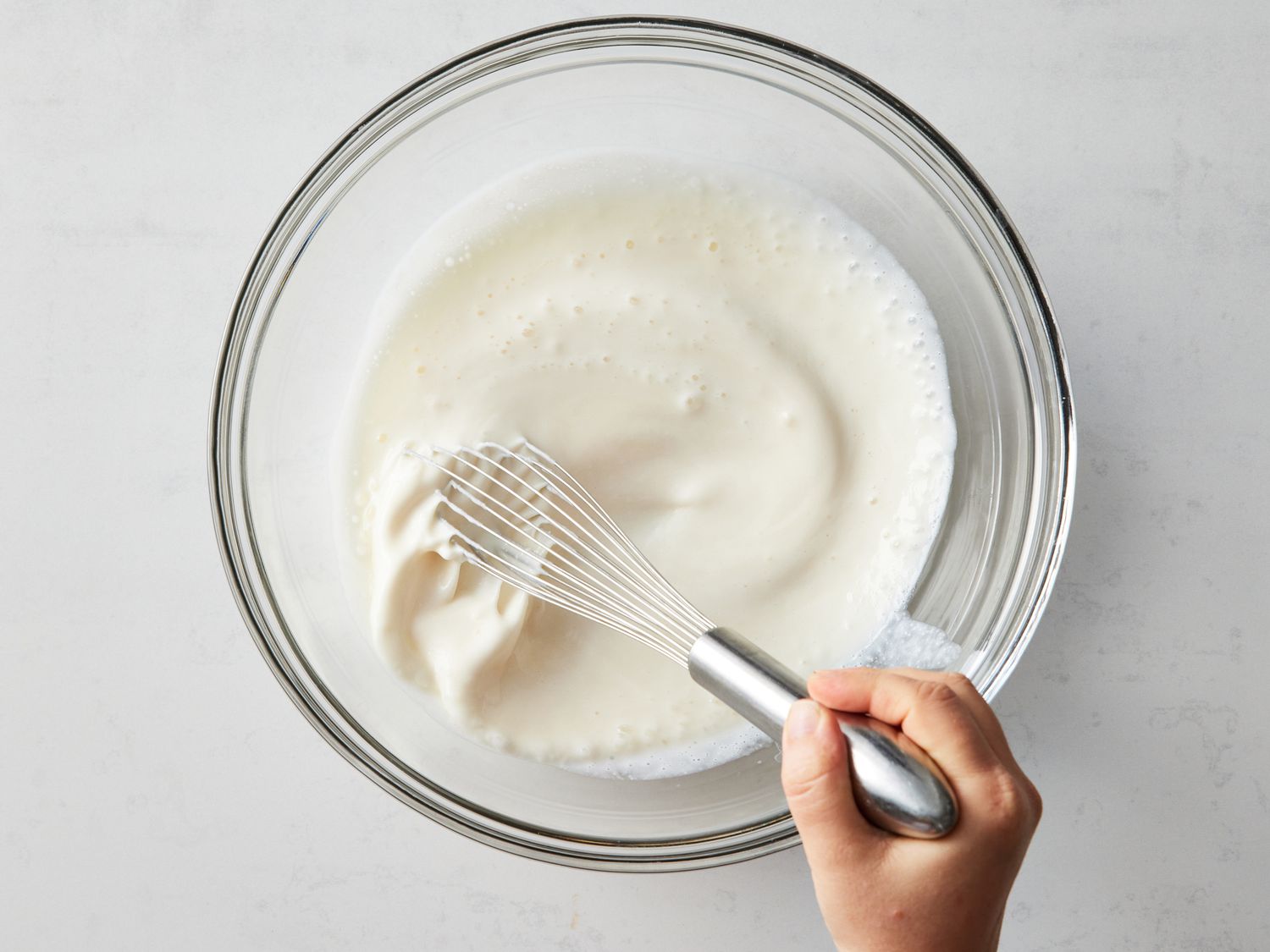 Hands stirring cottage cheese bread batter in a large mixing bowl on a bright kitchen counter with a rubber spatula
