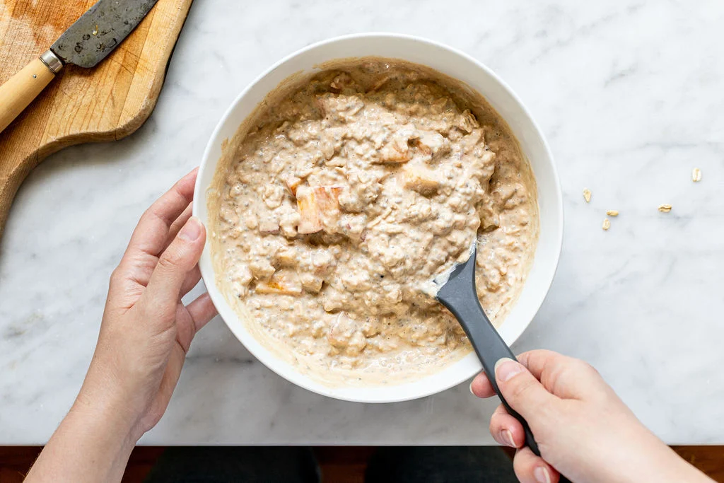 Hands stirring oats, yogurt, and milk together in a wide-mouth mason jar with a spoon