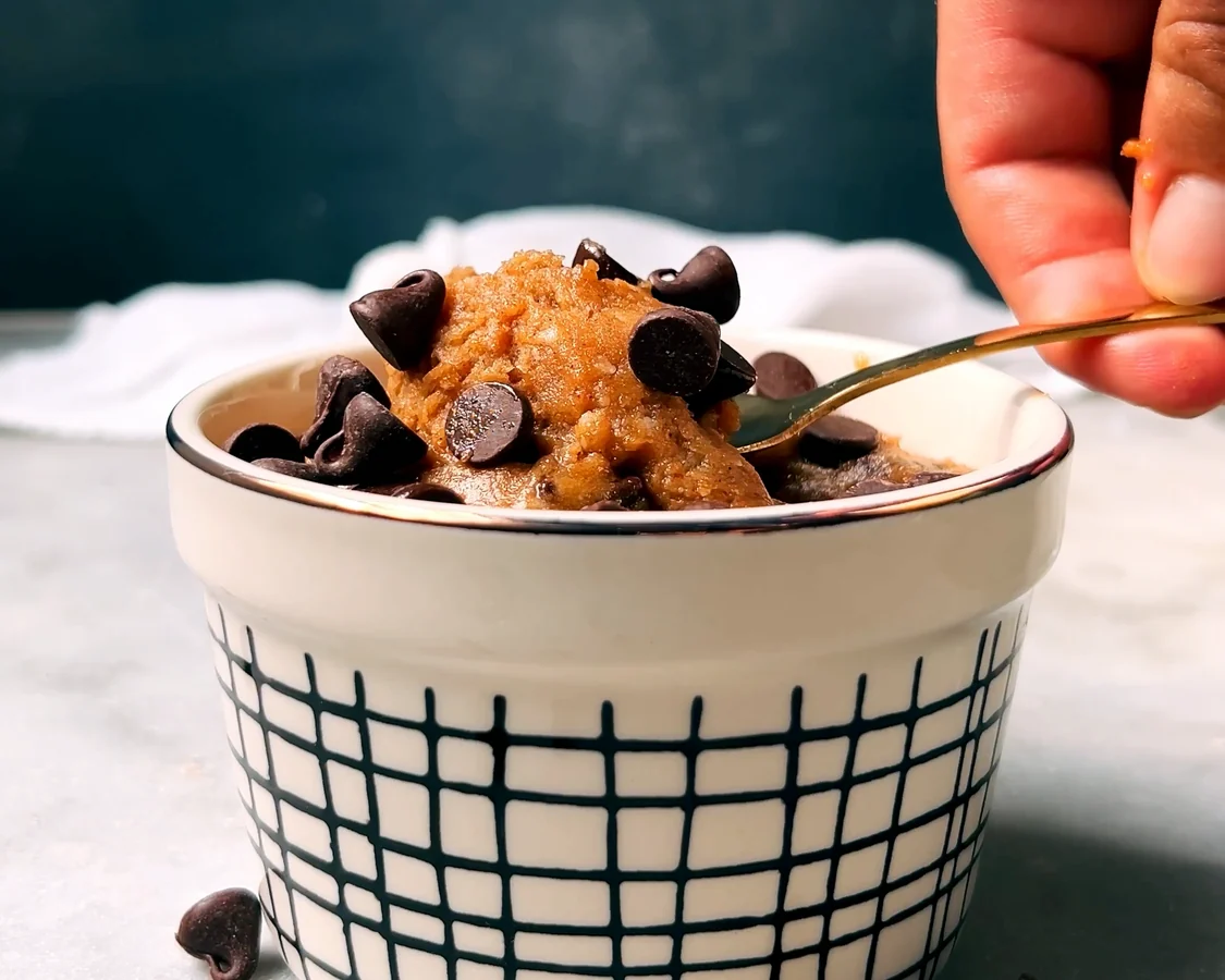 Hands stirring thick protein cookie dough in a large mixing bowl on a bright kitchen counter