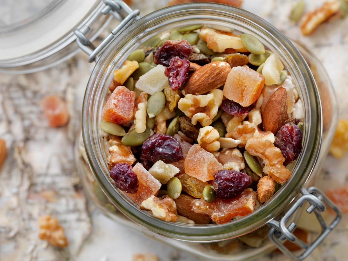 Hands stirring trail mix in a large white mixing bowl with a wooden spoon on a bright kitchen counter