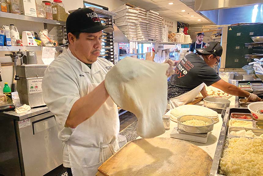 Hands stretching pizza dough into a round on a lightly floured kitchen counter