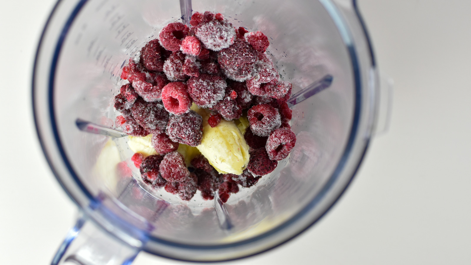 Hands tipping a bowl of frozen mixed fruit into a blender jar on a bright kitchen counter
