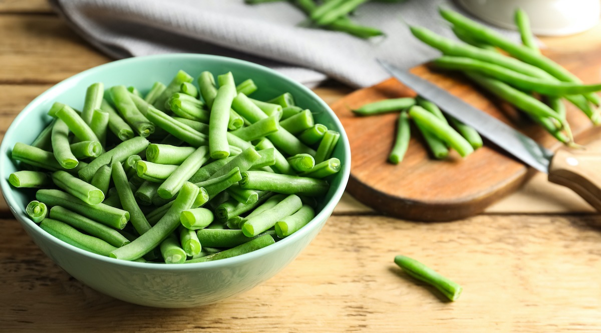 Hands trimming the stem ends from fresh snap beans on a wooden cutting board in a bright home kitchen