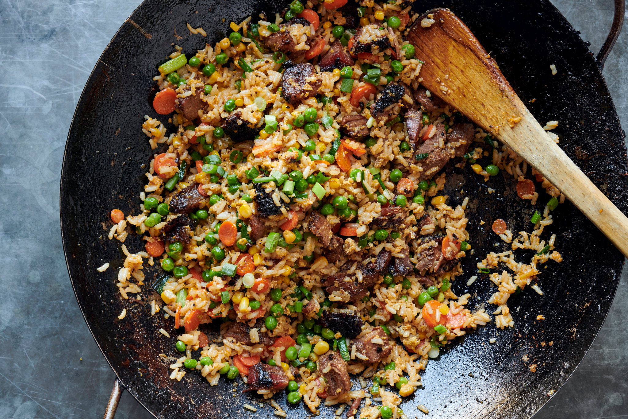 Hands using a spatula to toss fried rice in a hot skillet on a home stove, with visible steam and browned rice grains