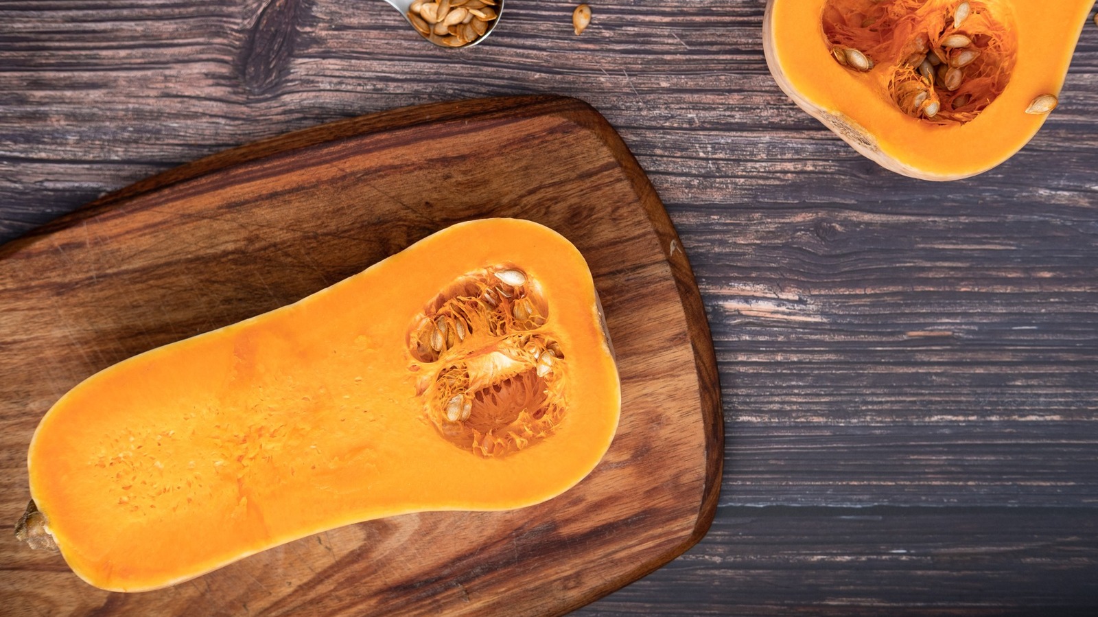 Hands using a spoon to scoop seeds from a halved pepper squash on a cutting board, with seeds gathered to one side