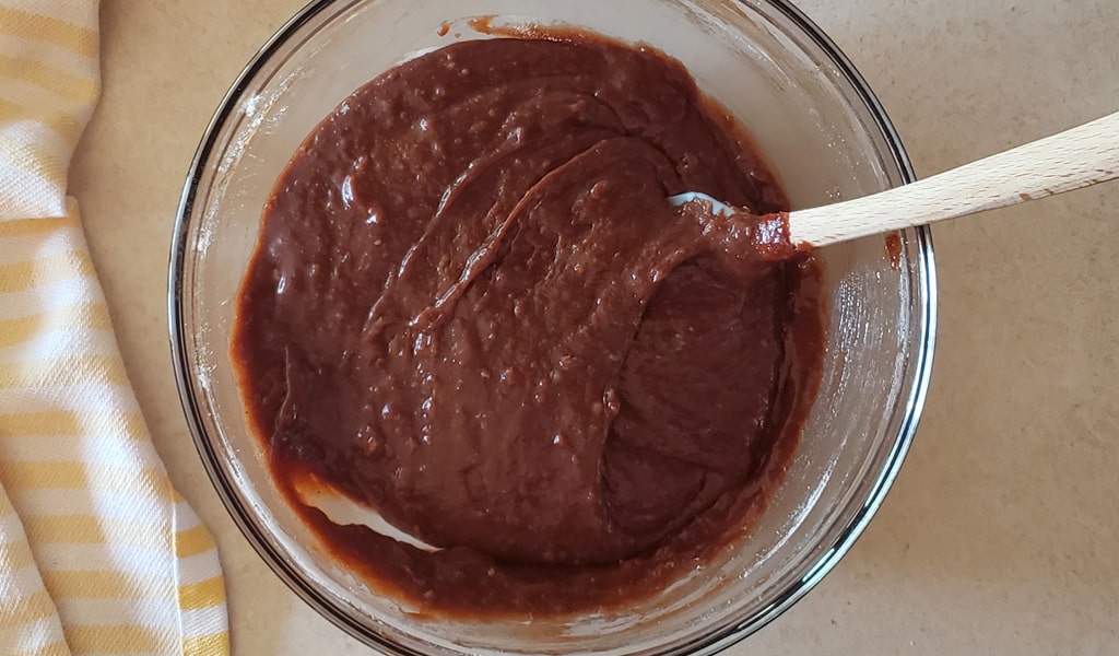 Hands whisking glossy brownie batter in a large mixing bowl