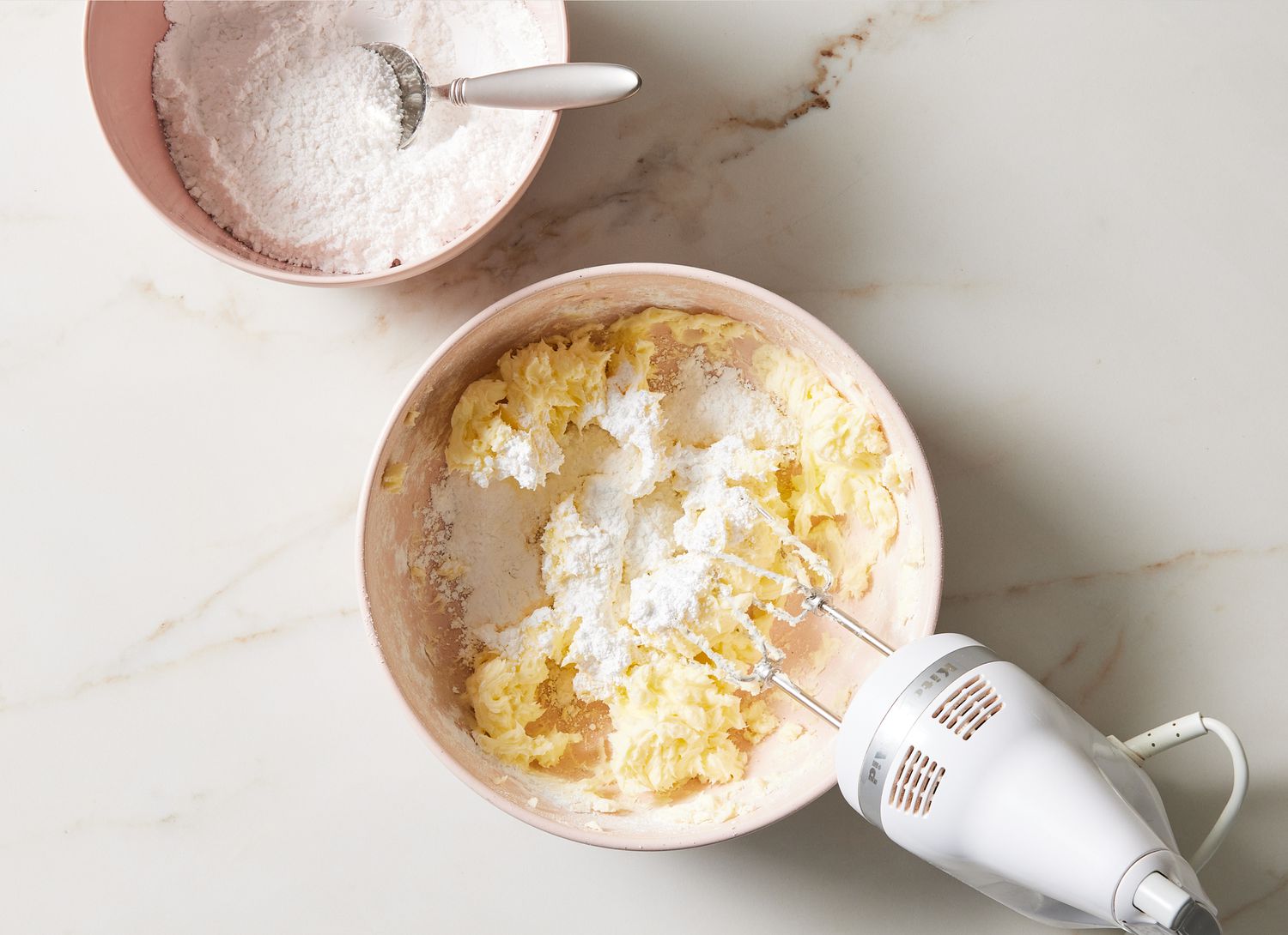 Hands whisking powdered sugar frosting in a mixing bowl on a bright kitchen counter