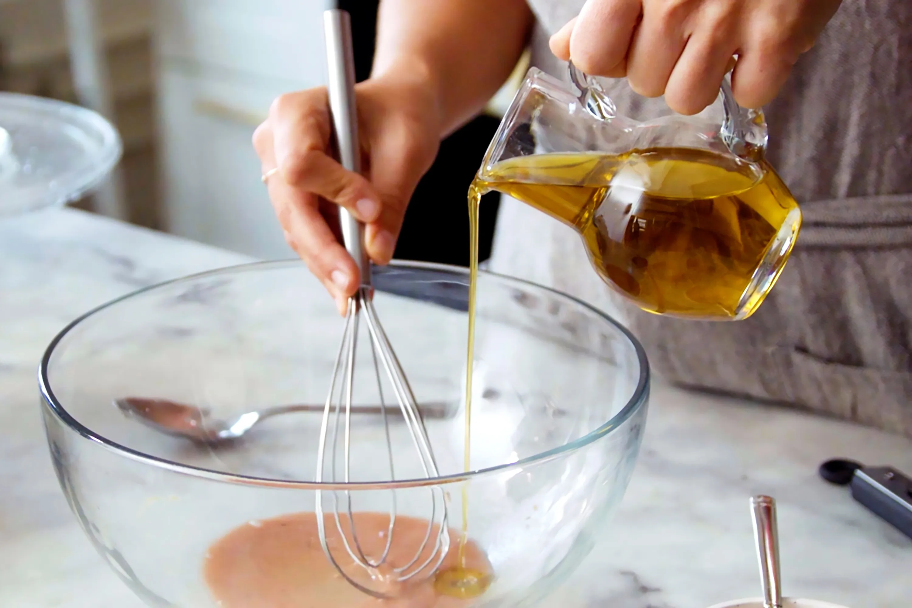 Hands whisking sesame ginger dressing in a small ceramic bowl on a bright kitchen counter