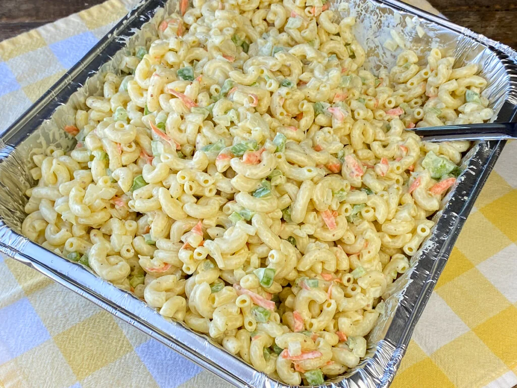 Hawaiian macaroni salad stored in a clear airtight container in a refrigerator, showing a creamy texture with grated carrot
