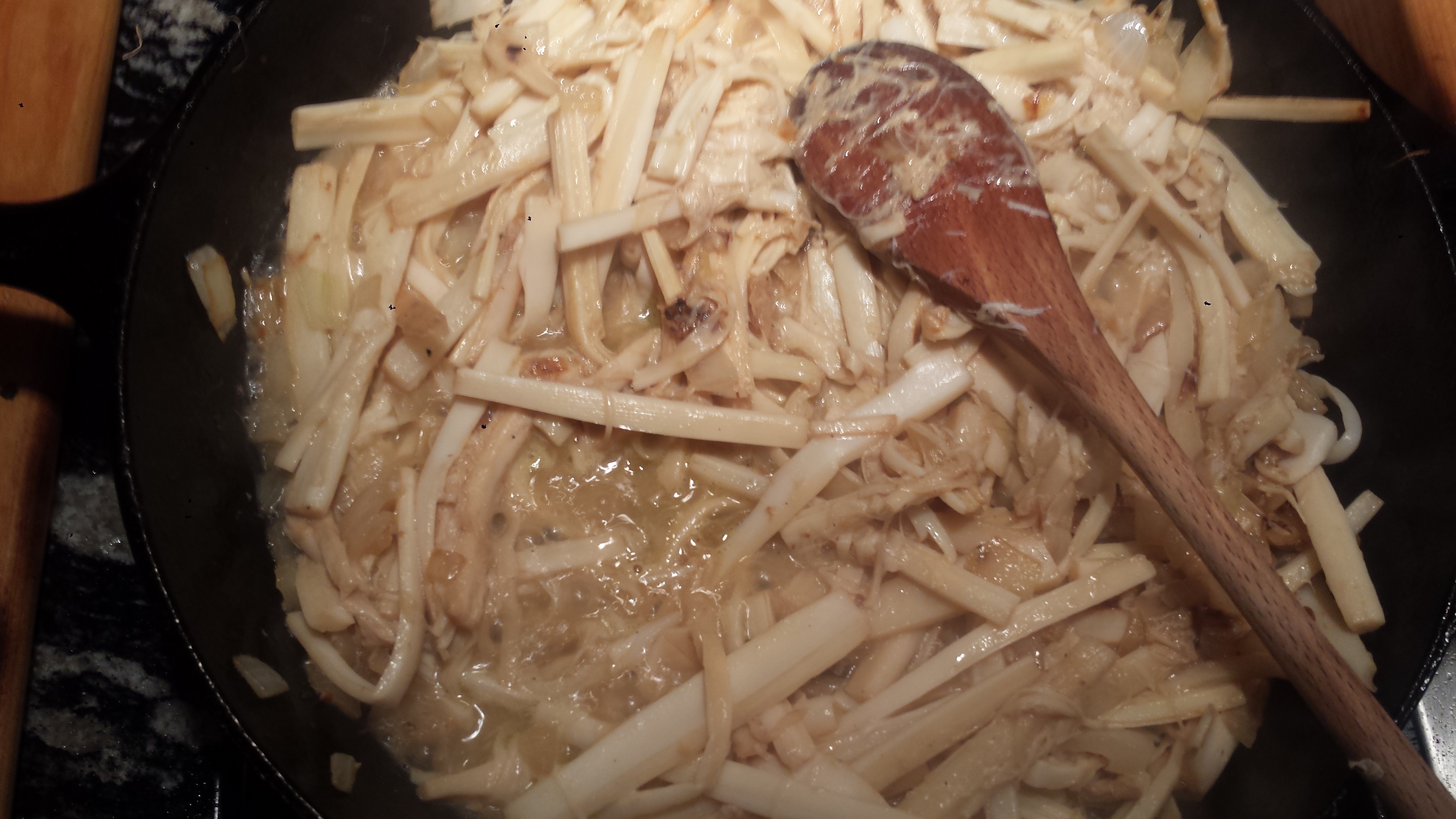 Hearts of palm being shredded in a mixing bowl with a fork on a kitchen counter, with a towel nearby for squeezing moisture