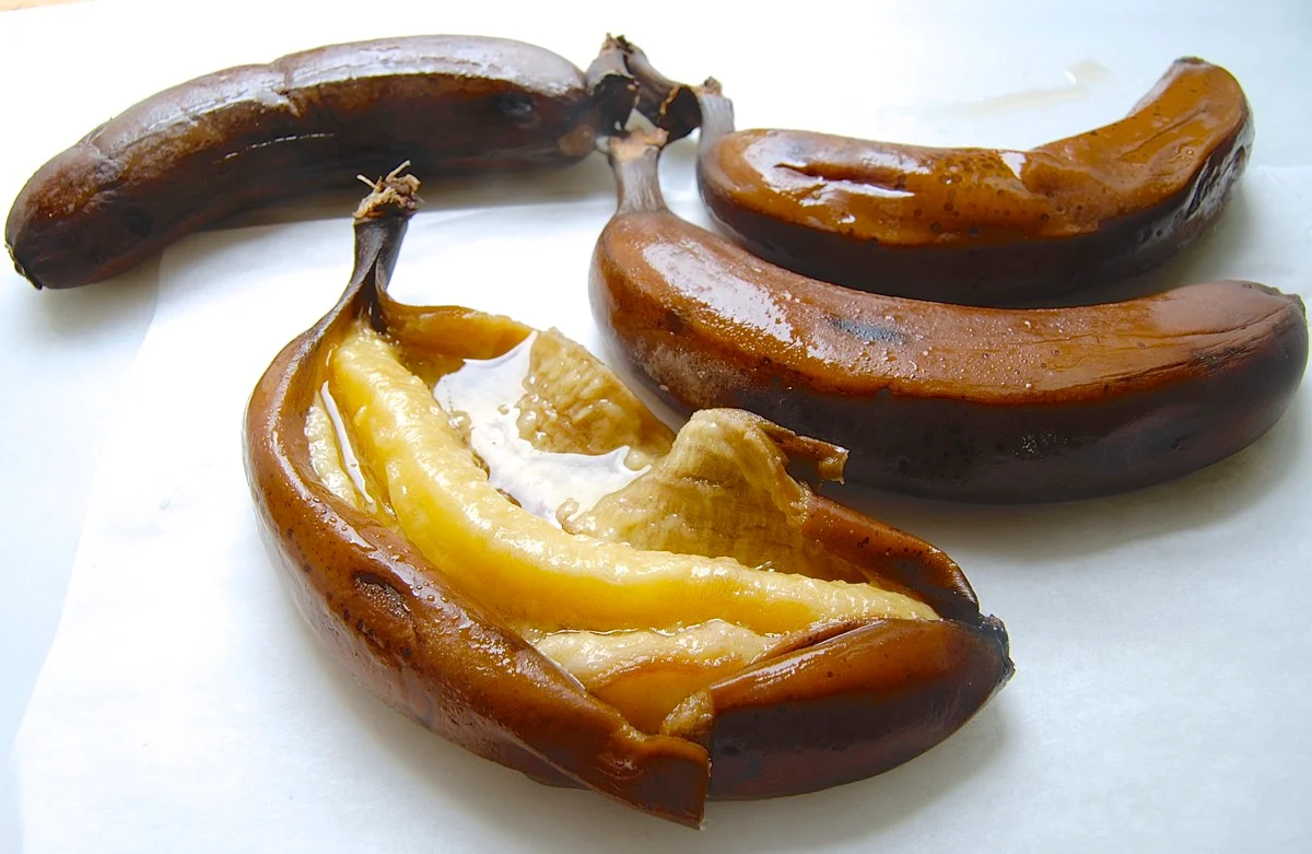 Heavily speckled ripe bananas on a kitchen counter beside a mixing bowl and a wooden spoon