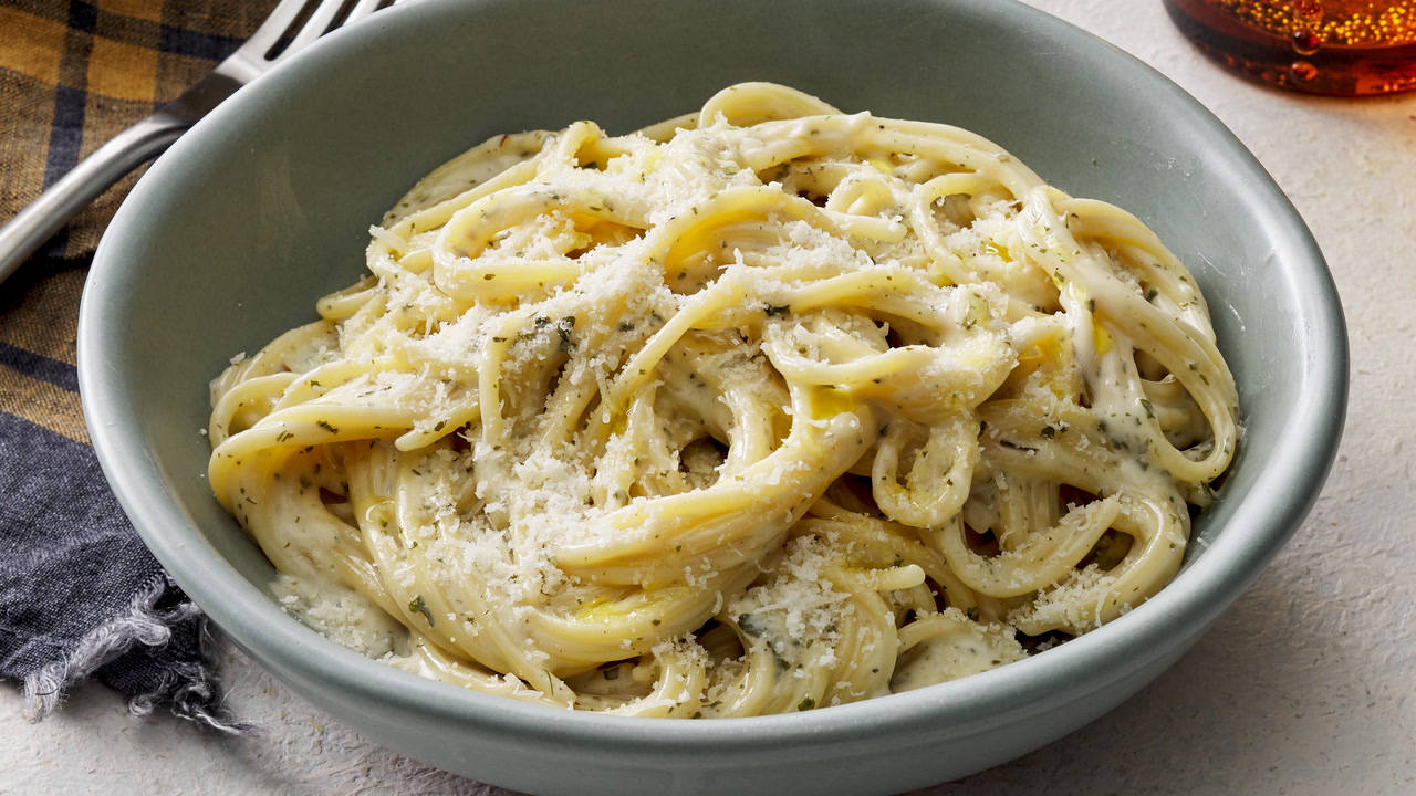 Heavy cream, butter, Parmesan cheese, garlic, and black pepper arranged on a clean kitchen counter with a saucepan nearby