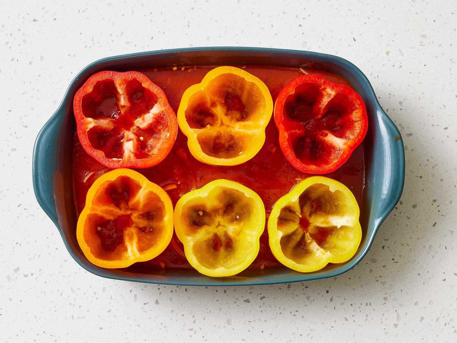 Hollowed bell peppers standing upright in a glass baking dish with a small amount of water in the bottom, ready to be pre-baked