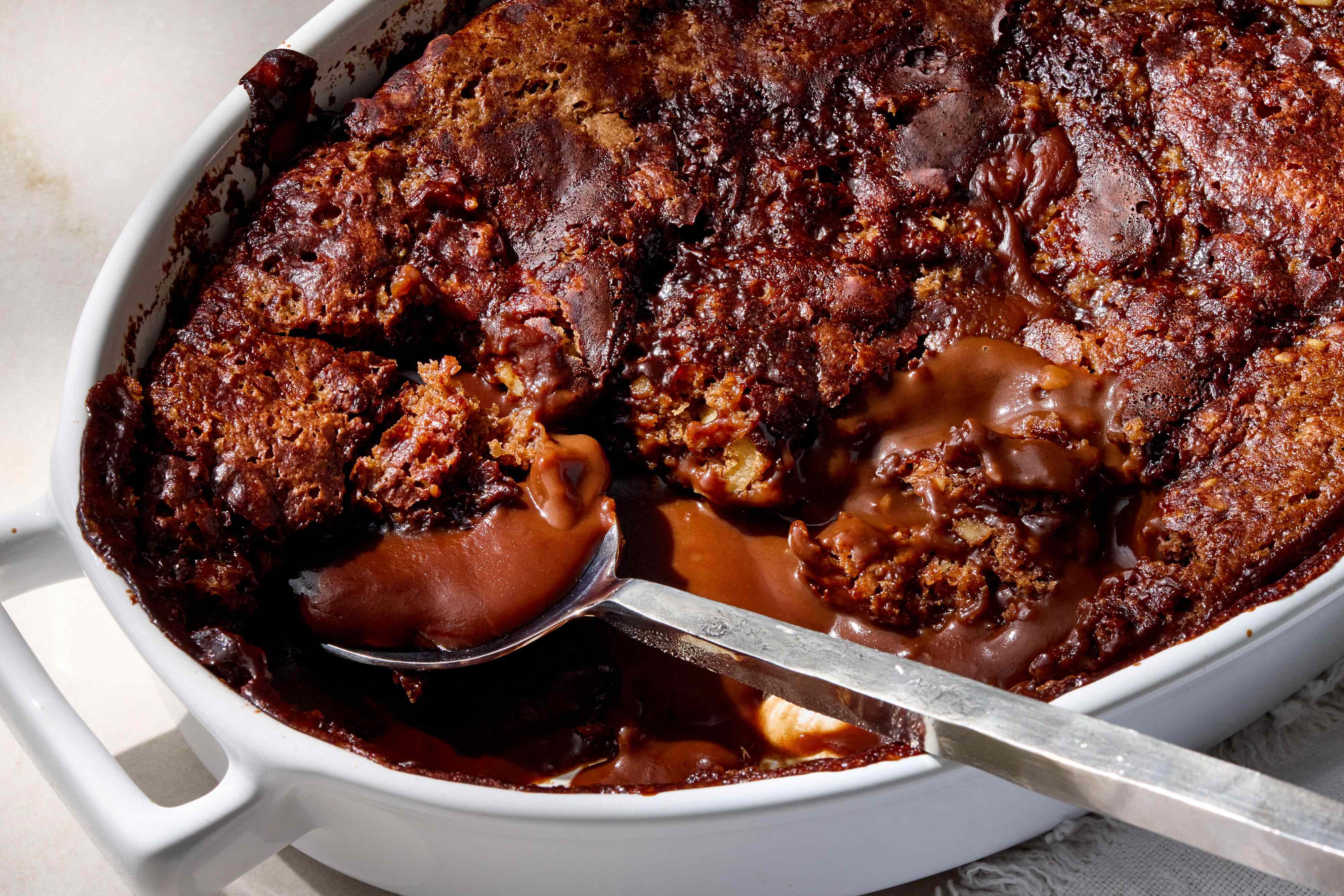 Hot water being carefully poured over a cocoa and brown sugar topping in a square baking dish before baking