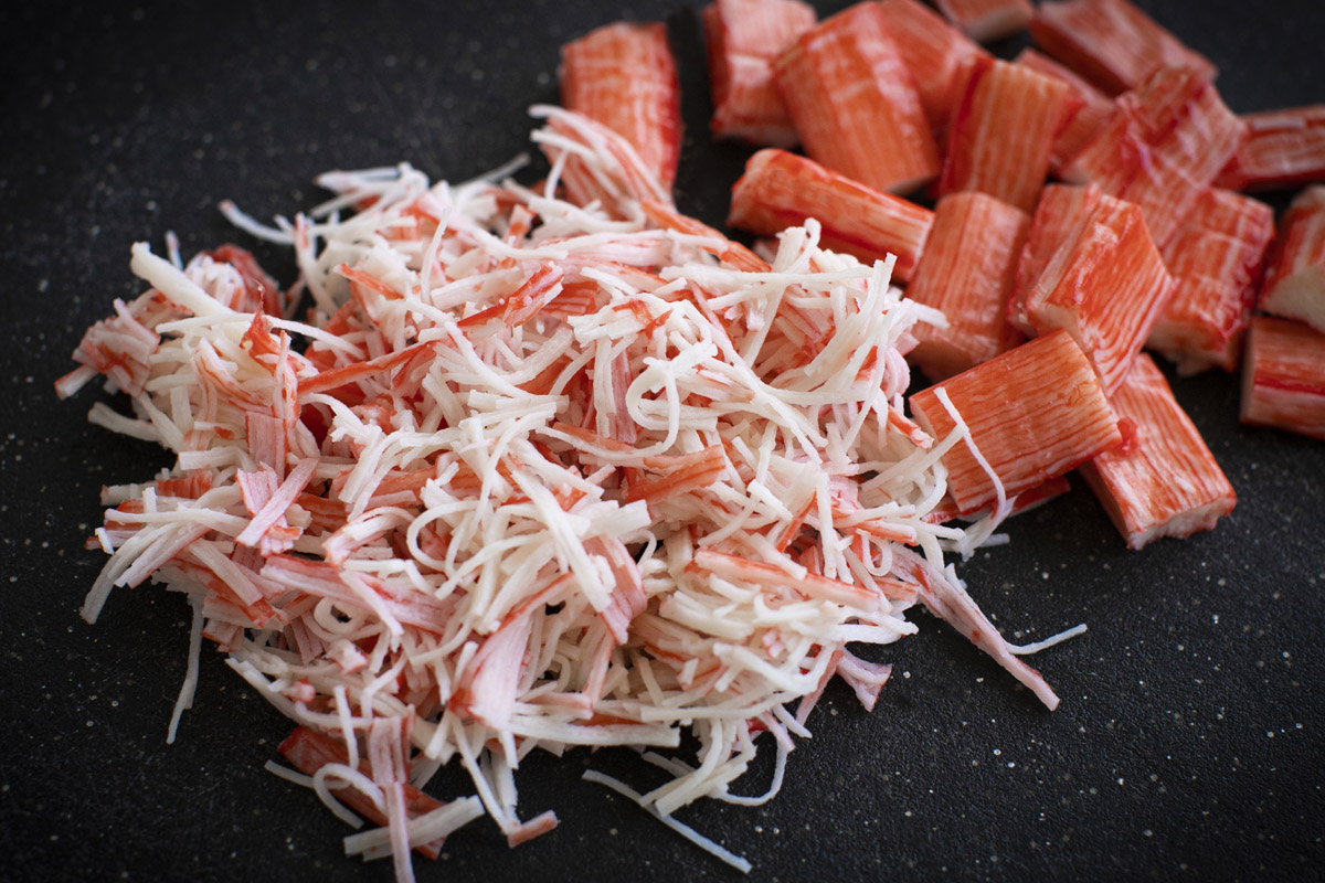 Imitation crab sticks shredded into thin strands in a mixing bowl