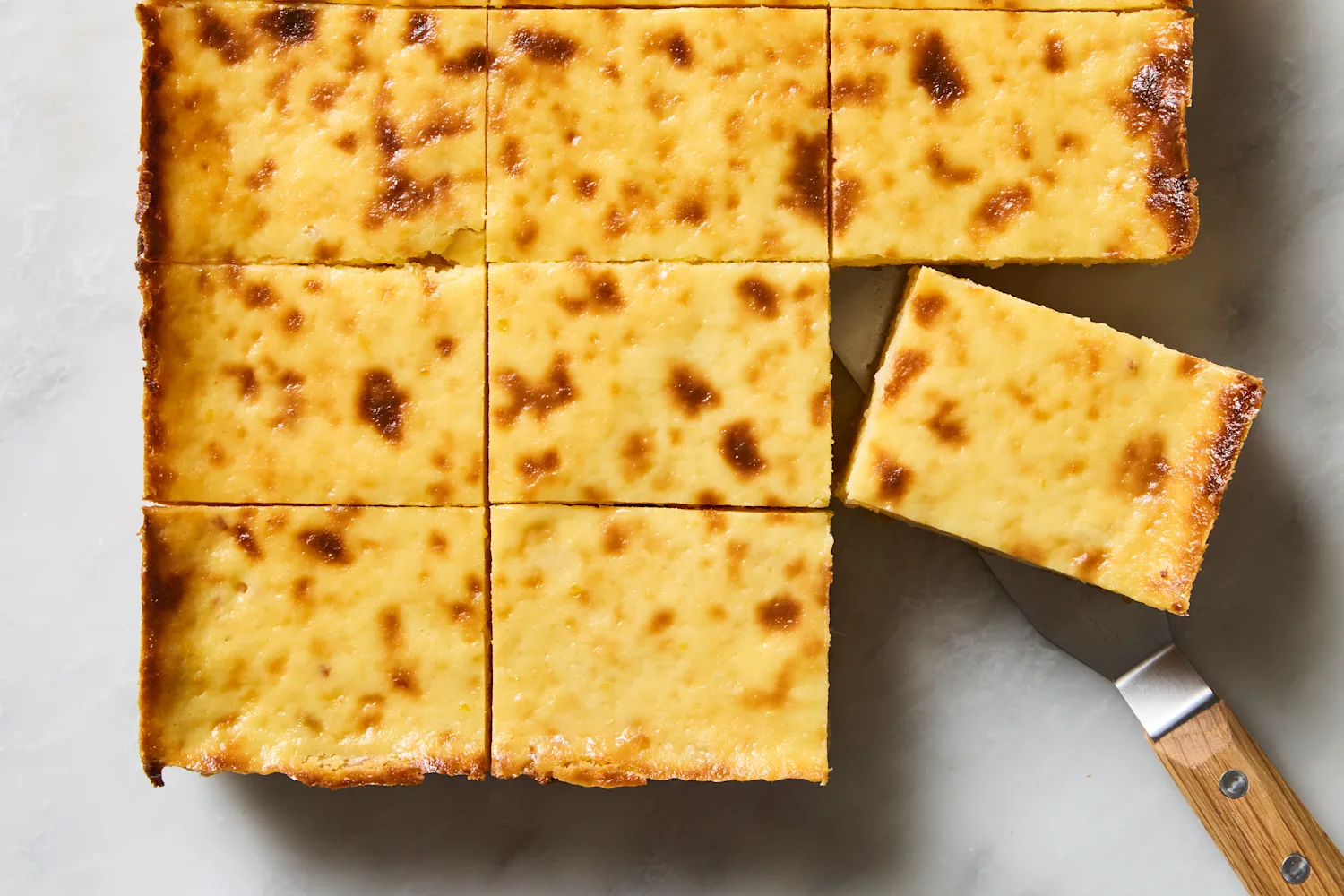 Individual cassava cake slices stored in a glass airtight container lined with parchment on a kitchen counter