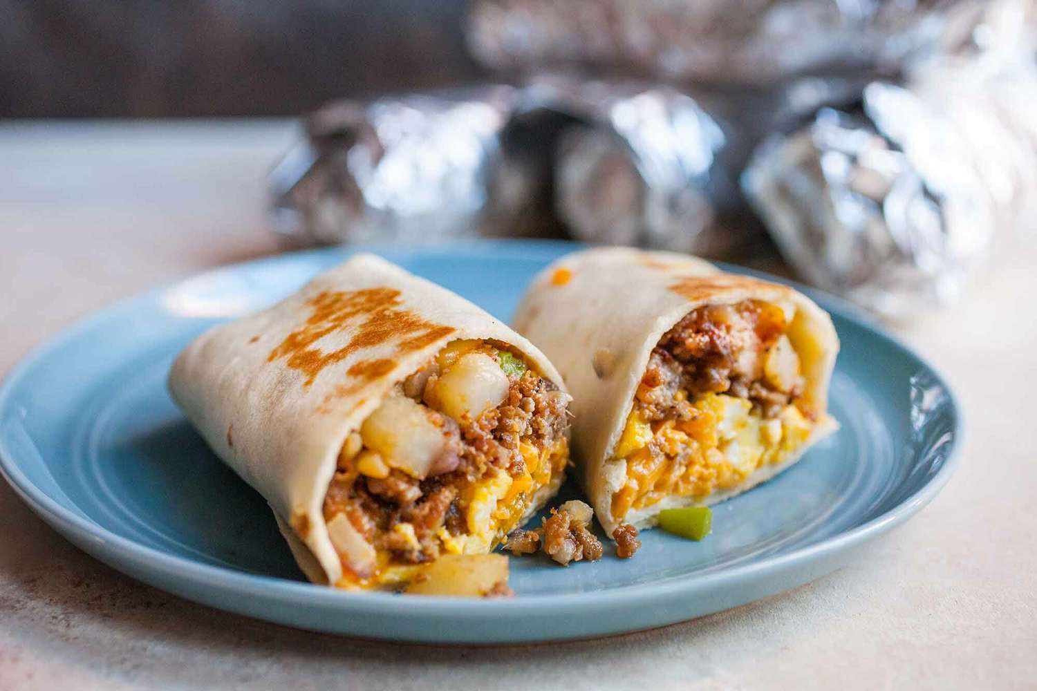 Individually wrapped breakfast burritos arranged in a single layer on a baking sheet ready to be placed in a freezer